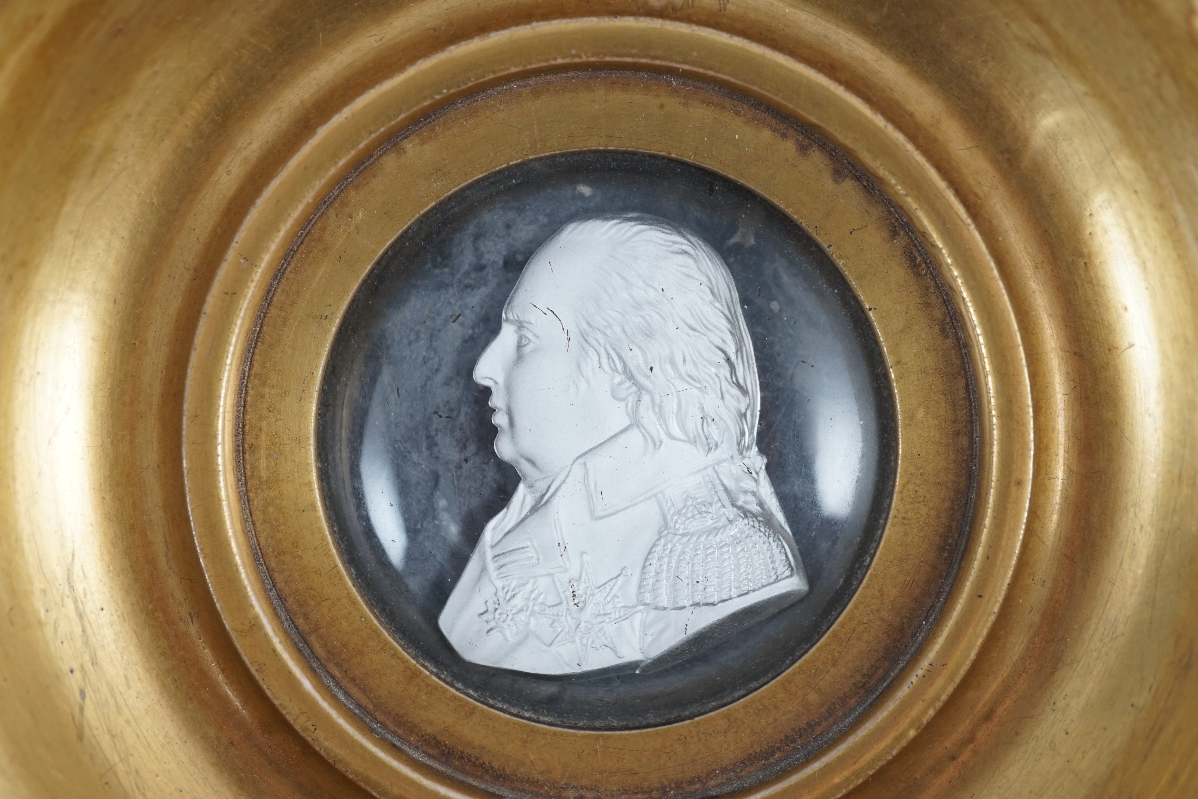 A Louis XVIII glass sulphide portrait plaque, in a gilded porcelain frame, c.1820, 14.5cm diameter